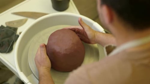 Over shoulder view male potter working raw clay material on studio pottery turntable wheel