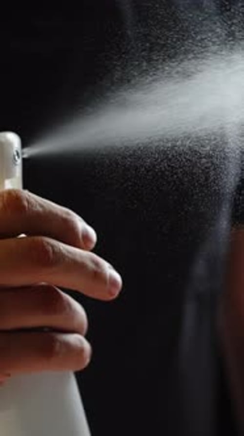 Gros plan d'une main appuyant sur la gâchette d'un flacon pulvérisateur blanc libérant une fine brume dans l'obscurité