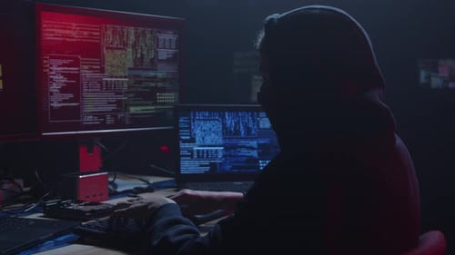 Un misterioso hacker está presente en una habitación oscura rodeada de múltiples pantallas