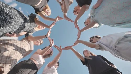 Group of Friends Standing in Circle Joining Hands Together Against Blue Sky Low Angle View