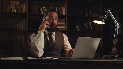 Bearded Man Talking on the Phone While Working on a Laptop Male Businessman Sitting in His Office