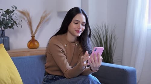 Smiling Woman Using Smartphone on Couch Indoors