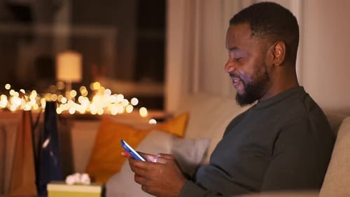 Man Using Smartphone at Home with Christmas Lights