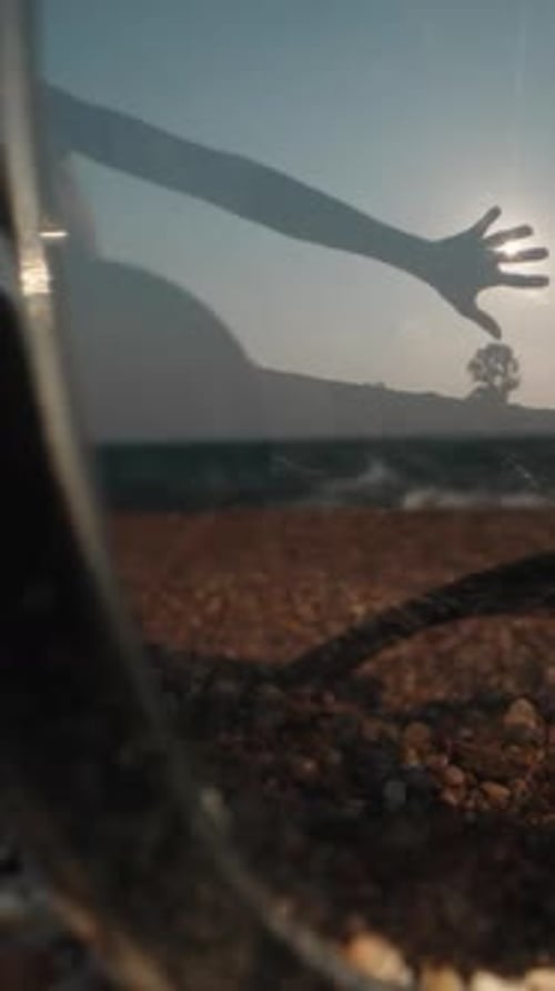 Sunglasses lie in the sand against the background of the sea. The hand covers the sun in reflection.