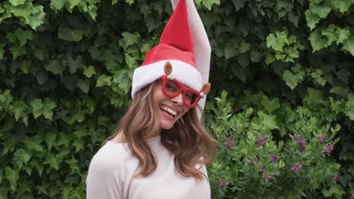 Woman in Santa Hat Dances in Front of Greenery