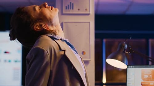 Woman Stretches Back at Office Workstation at Night