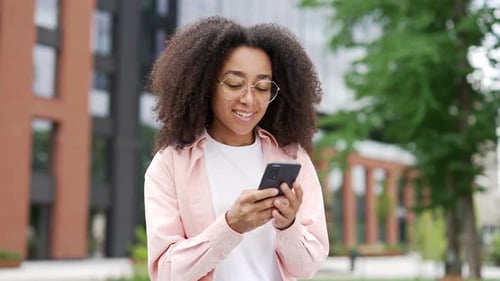 Smiling african american female student using smartphone standing in campus space near university