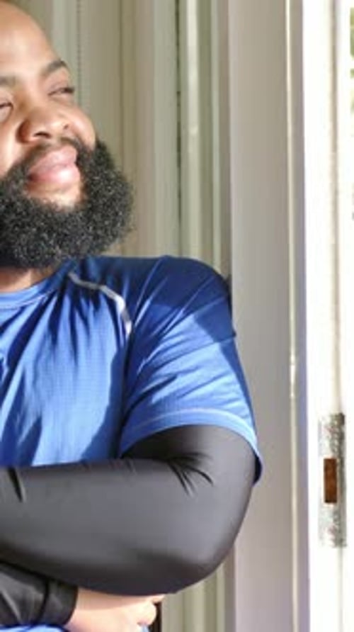 Vidéo verticale : La lumière du soleil dessine un homme en chemise bleue et manches noires regardant une porte, espace de copie
