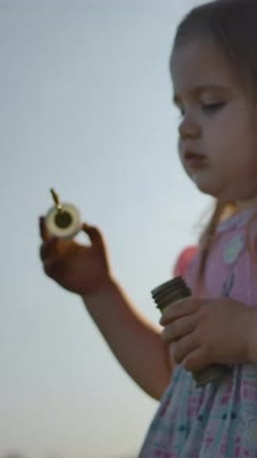 Vertical of Side View of Little Girl in Blows Soap Bubbles on the Nature