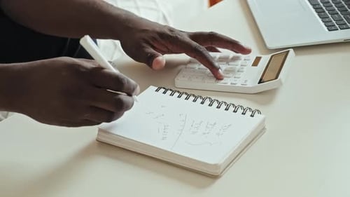 Hands calculate and write in notebook at desk