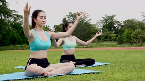 Two beautiful young woman sit meditation doing yoga in park. Relaxing and meditating while being sur