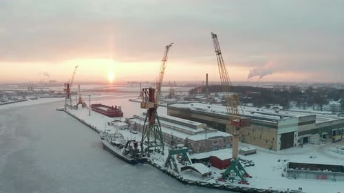 Aerial view of industrial port in winter, covered with show, frozen water. Beautiful golden sun ligh