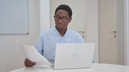 Young Adult Man Works with Laptop and Papers