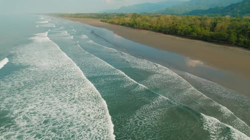 Ocean waves rolling gently toward empty dark sandy tropical beach in Costa Rica