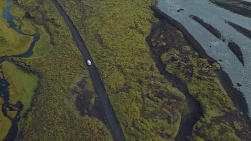 Top-down aerial view of white off-road car moving along the clear blue river stream.