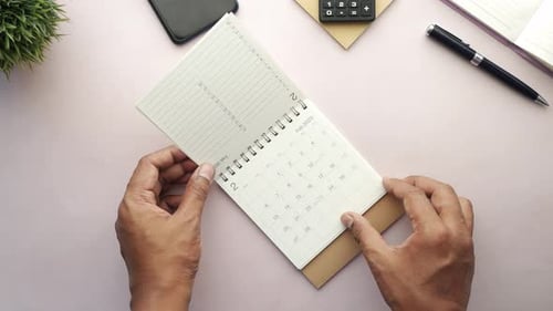 Person Hand Turning a Calendar on Table