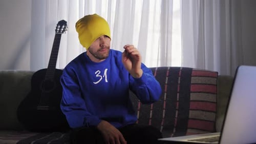 Man Sits on Couch Talking to Laptop Screen
