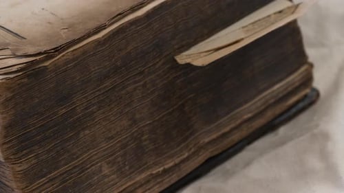 Close pan along ancient heavy worn bible in Swedish on white sheet
