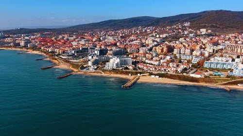 A seaside town situated next to the water. Buildings line the shore with a backdrop of hills.