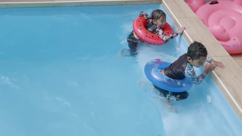 Happy young boy on inflatable ring having fun jumping in water and enjoys summer vacation in pool
