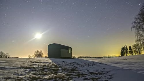 Timelapse of a snowy landscape with a wooden cabin over which the milky way in the starry sky at dus