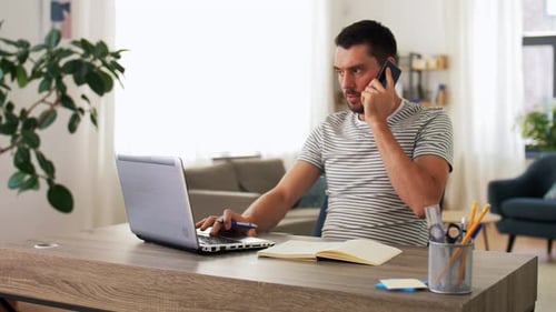 Man using Laptop talking on phone at desk