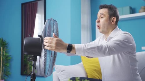 Overwhelmed by the heat, the man is holding the fan to himself.