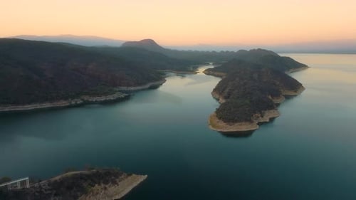 Aerial drone flying over a lake, water dam, with mountains at sunrise. Beautifull dreamy landscape