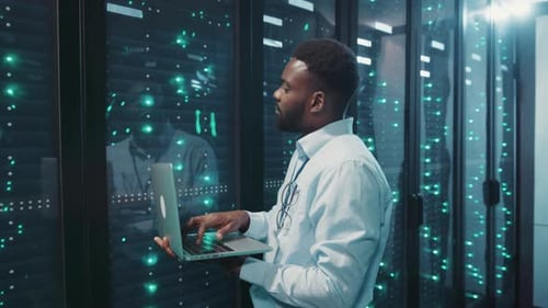 A Man Works on a Laptop in a Hightech Server Room Showcasing IT Expertise