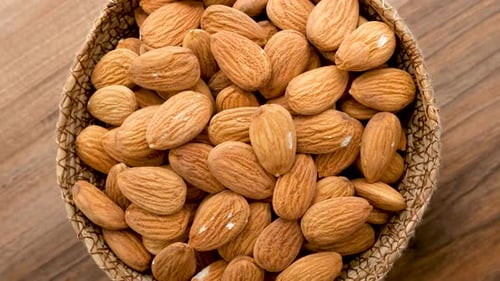 Close Up View Of A Wicker Bowl Filled With Peeled Almonds Rotates On A Wooden Surface