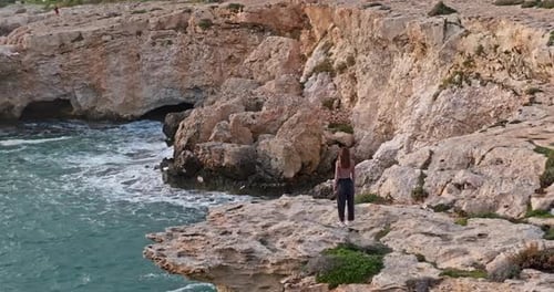Aerial View of a Woman Standing on a Rocky Shore of the Ocean