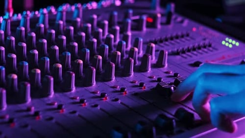 Sound Engineer Moves Faders Up and Down on Audio Mixer in Neon Light CloseUp