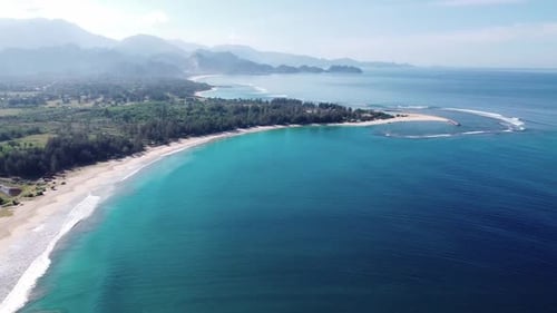 Aerial view of tropical beach and sea water with small waves close to mountains.