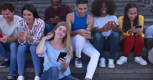 Happy diverse millennial friends using mobile phones in the city