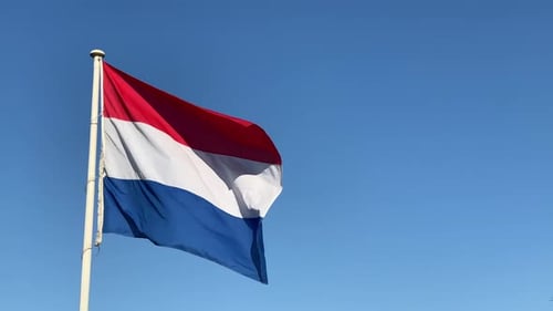 Netherland flag blowing in the wind with a clear blue sky background during the day.