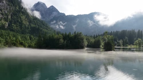 Aerial View of a Misty Alpine Lake with Mountains and Forest in the Background