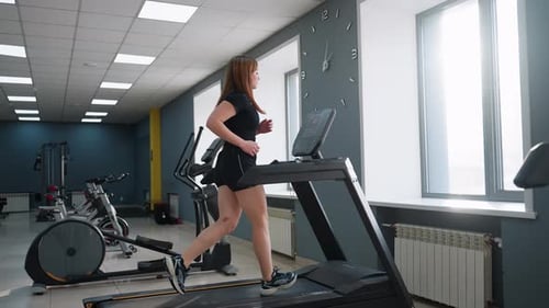 Side View of Woman Running Fast on Treadmill in Sunlit Gym