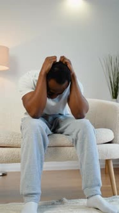 Worried Man Sits on a Couch With Hands on Head