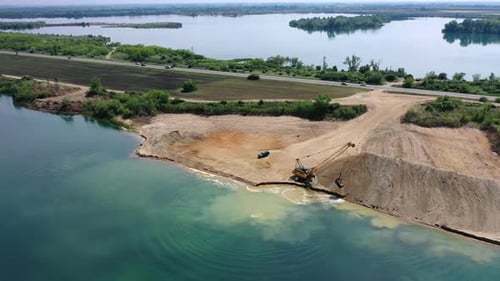 Overview of a quarry work site yellow excavator moving sand. Blue water lake.