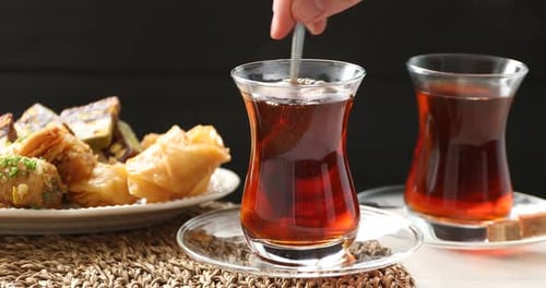 Woman adding and stirring brown sugar in glass cup with Turkish tea at table, closeup