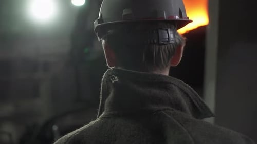 Person Observing Molten Metal in Dark Factory