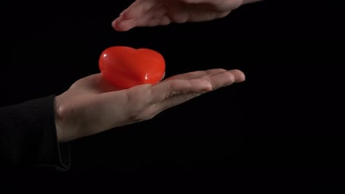 Hand Presents Red Heart on Black Background