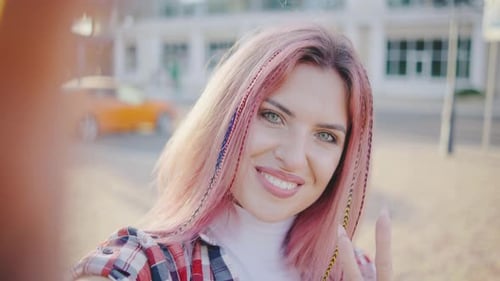 Beautiful Young Hipster Woman with Pink Hair Takes a Selfie in the Park or on the Street at Sunset