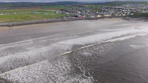 Ocean Waves Crashing On The Shoreline Of Lahinch Beach With The Town In The Distance In Ireland. - a