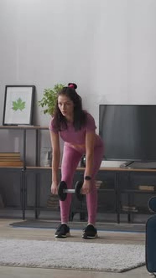 Focused Young Woman in Pink Sportswear Performing Dumbbell Workout at Home Building Strength and