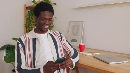 Happy Young Man Using Mobile Phone While Sitting at Home Office Workplace