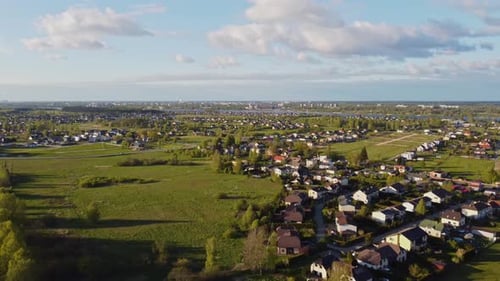 Slow drone pull away over Katlakalns residential area, green open fields and distant Riga skyline