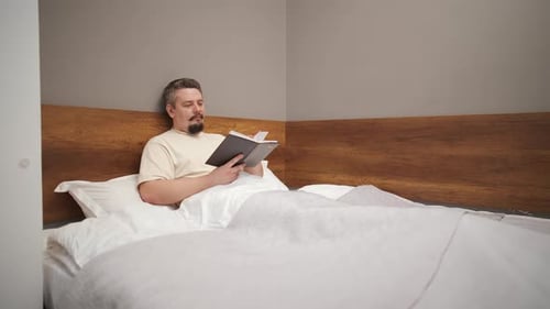 Middleaged Man Relaxing in Bed and Reading a Book