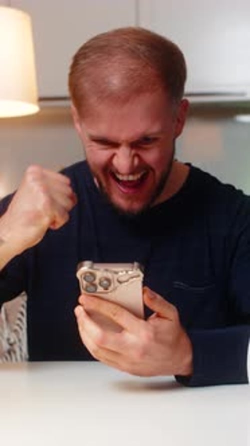 Man Cheering While Looking at Phone Indoors