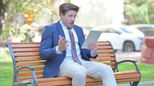 Surprised Businessman Using Tablet in Park